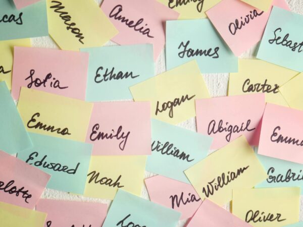 Closeup of paper stickers with different names on white wall. Concept of choosing baby name